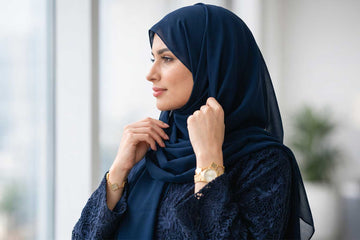 Woman in Sapphire Dantel navy lace abaya with matching navy chiffon sheila adjusting hijab with Dubai skyline at Layaal Abaya Studio