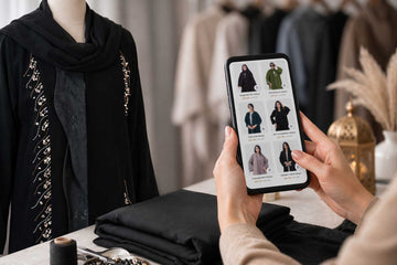 Woman browsing Layaal's handcrafted abaya collection on her phone beside the Noir Cascade Abaya on a mannequin in the Dubai atelier - Layaal