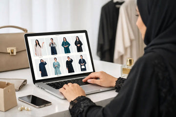 Woman in abaya browsing luxury abaya collection on laptop at Layaal